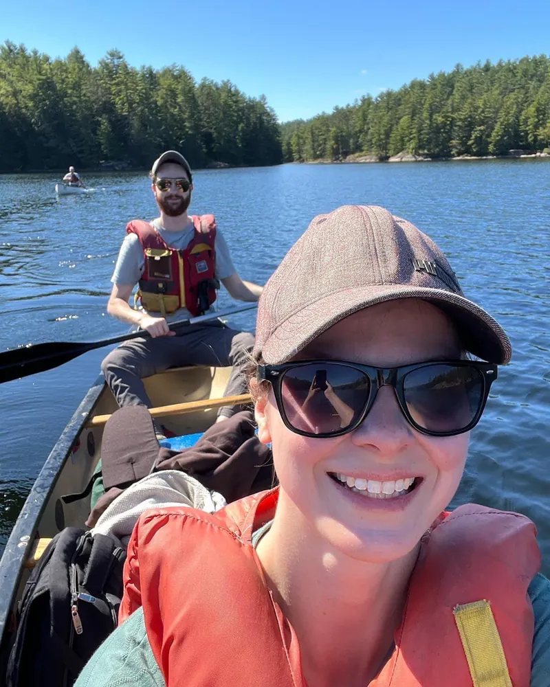 Two people in life jackets paddling a canoe on a calm tree-lined lake.