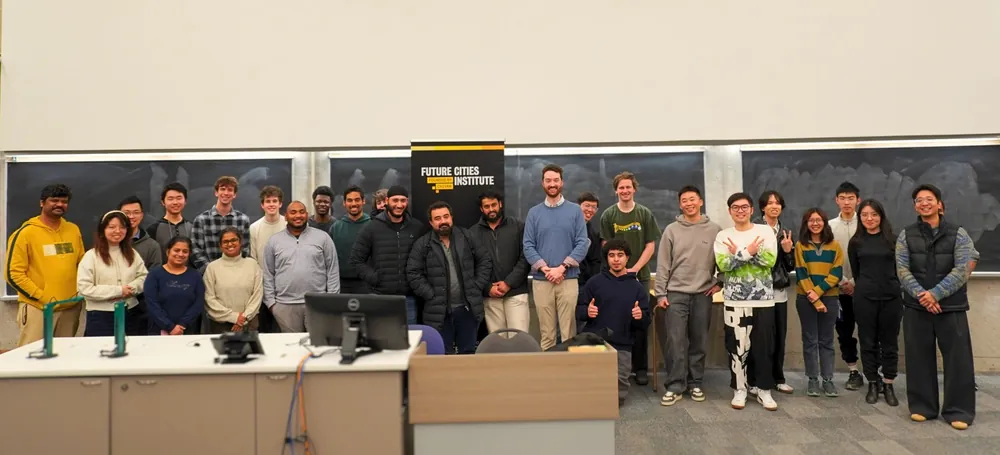 A large group of participants posing with a Future Cities Institute banner after a hackathon.