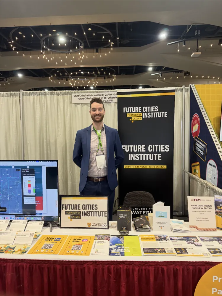 Skyler in a blue suit behind the Future Cities Institute booth at the FCM conference.