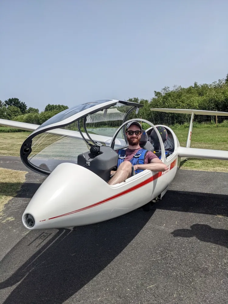 Skyler sitting in the open cockpit of a white glider on a runway.