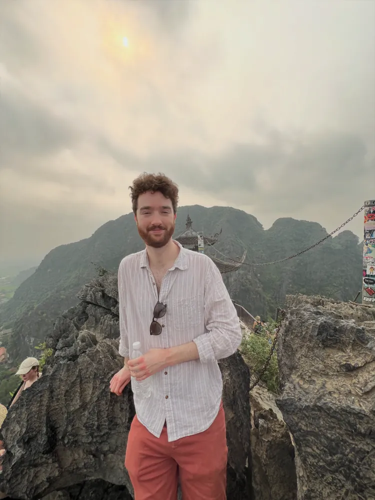 Skyler at the rocky Hang Mua viewpoint with limestone peaks and a pagoda behind him.