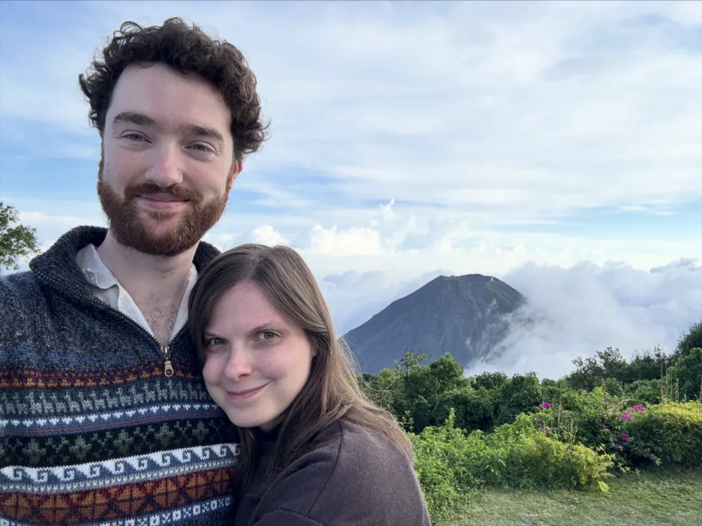 Skyler and his partner smiling above the clouds with a volcano peak behind them.